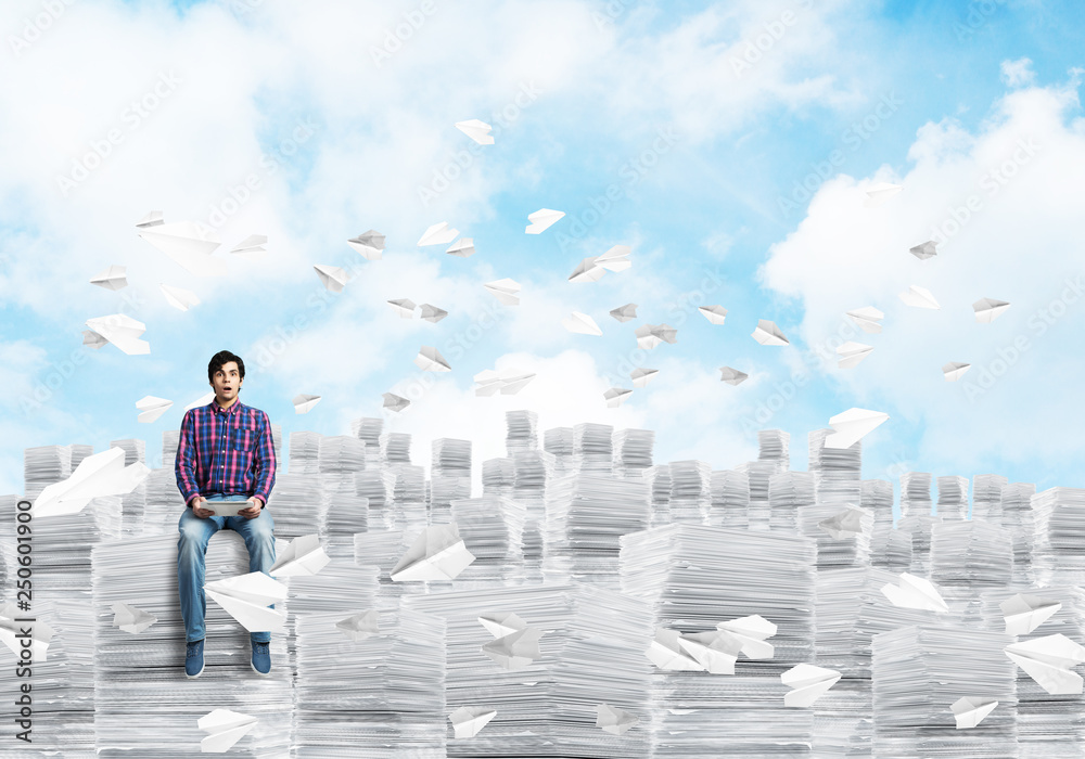 Attractive man sitting on pile of paper documents.