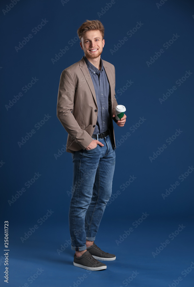 Fashionable young man with cup of coffee on color background