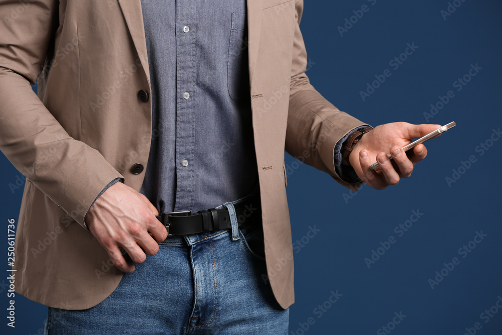 Fashionable young man with mobile phone on color background, closeup