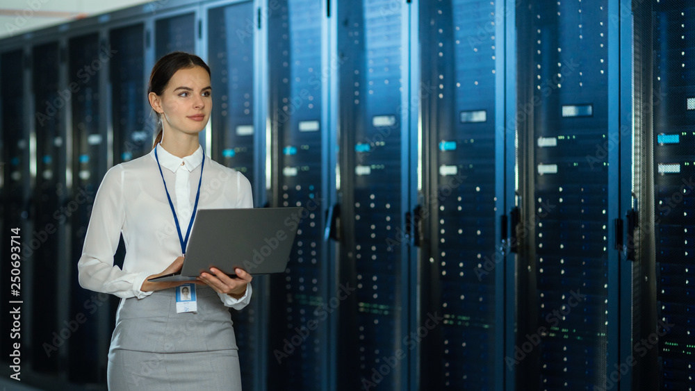 Beautiful Data Center Female IT Technician Walking Through Server Rack Corridor with a Laptop Comput