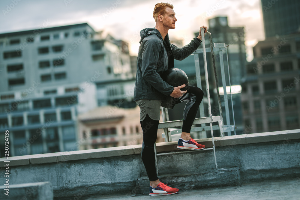 Fitness man standing on rooftop holding a medicine ball