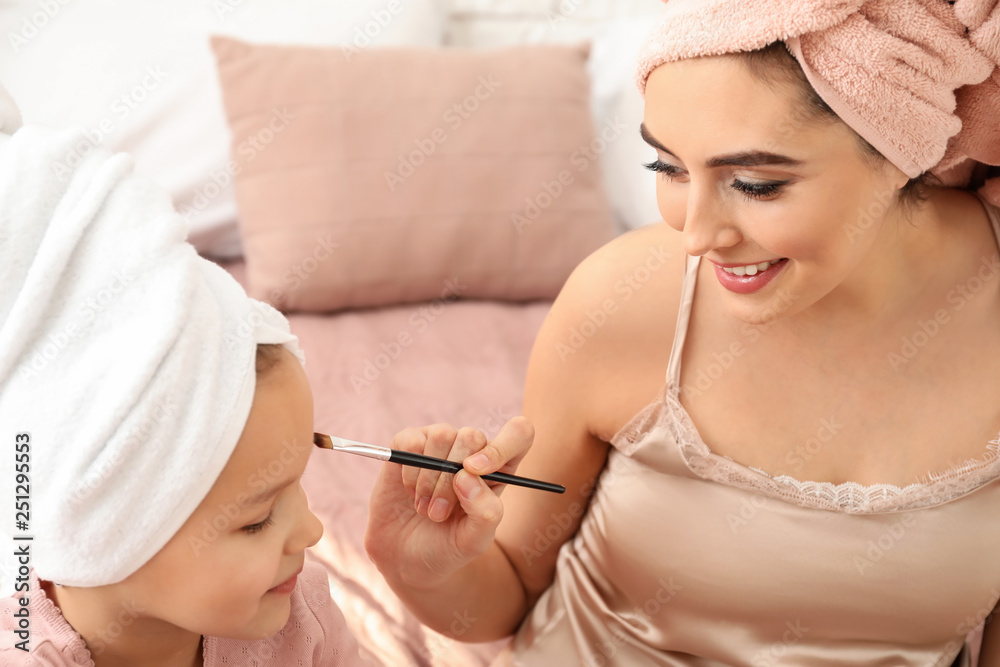 Young mother applying cosmetics onto face of her cute daughter at home