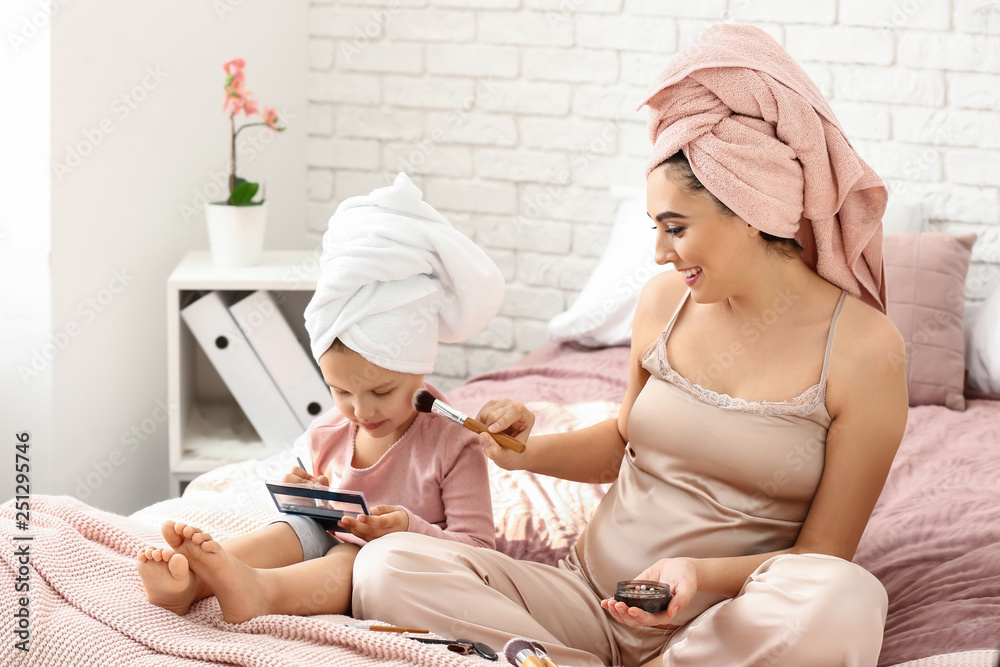 Cute little daughter and her mother with makeup cosmetics at home