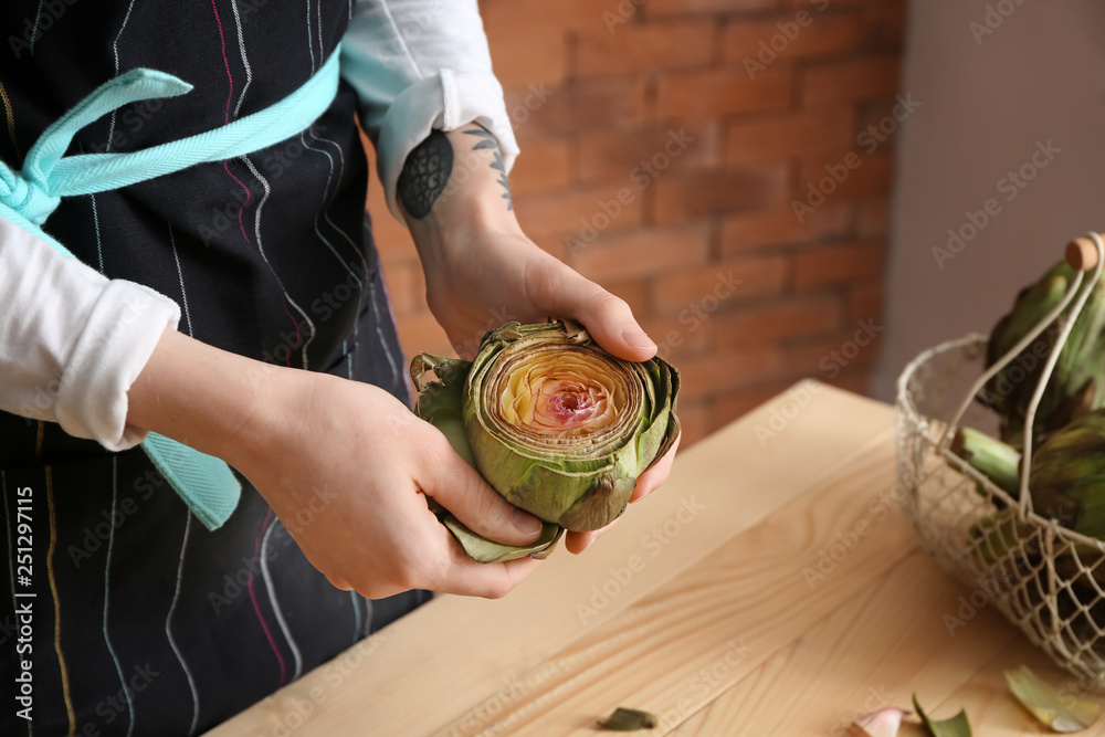 Woman preparing tasty raw artichokes in kitchen