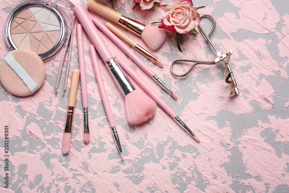 Professional makeup brushes with cosmetics on color background