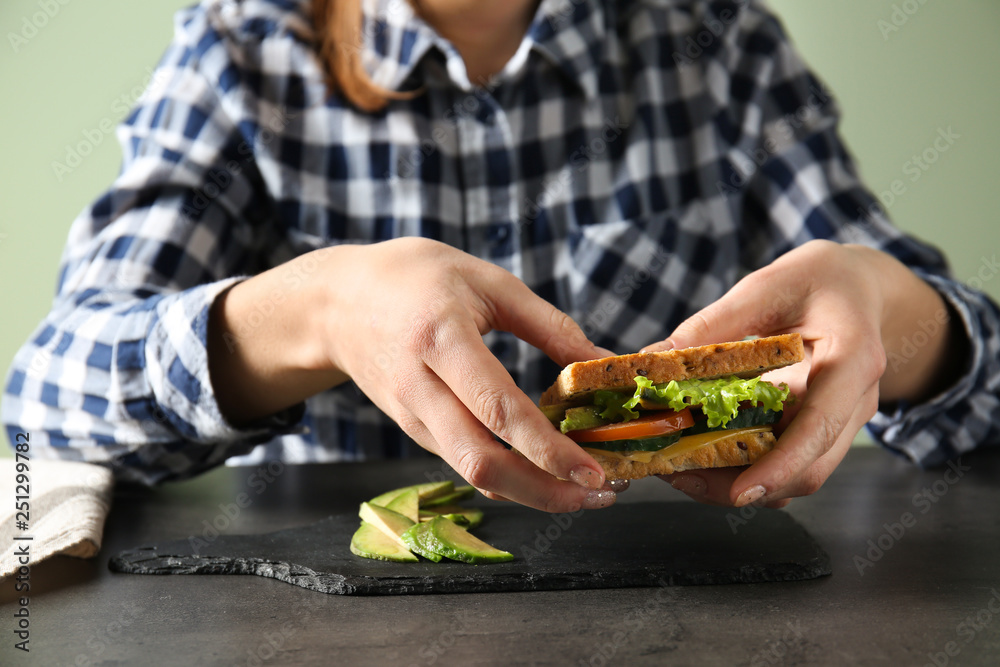 Young woman eating tasty sandwich with avocado at table, closeup