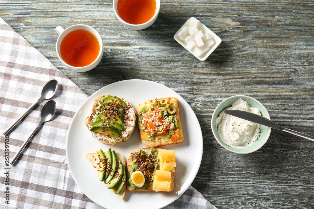 Plate with different tasty sandwiches and tea on wooden table