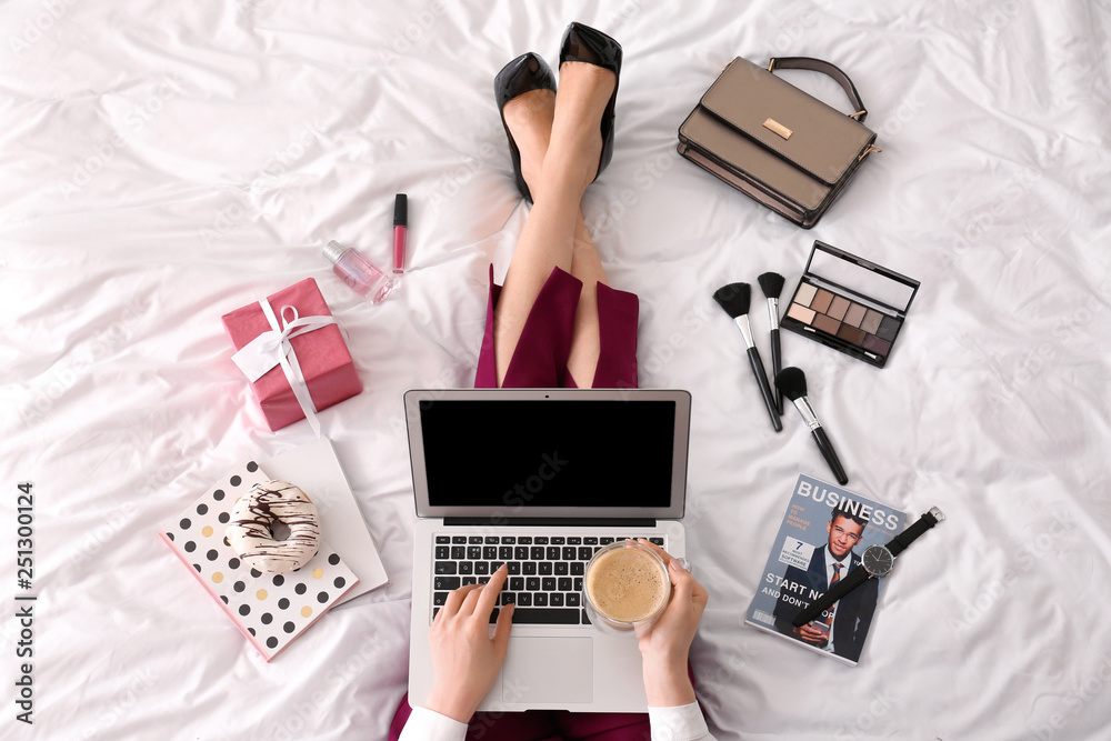 Young businesswoman with laptop drinking coffee on bed in morning