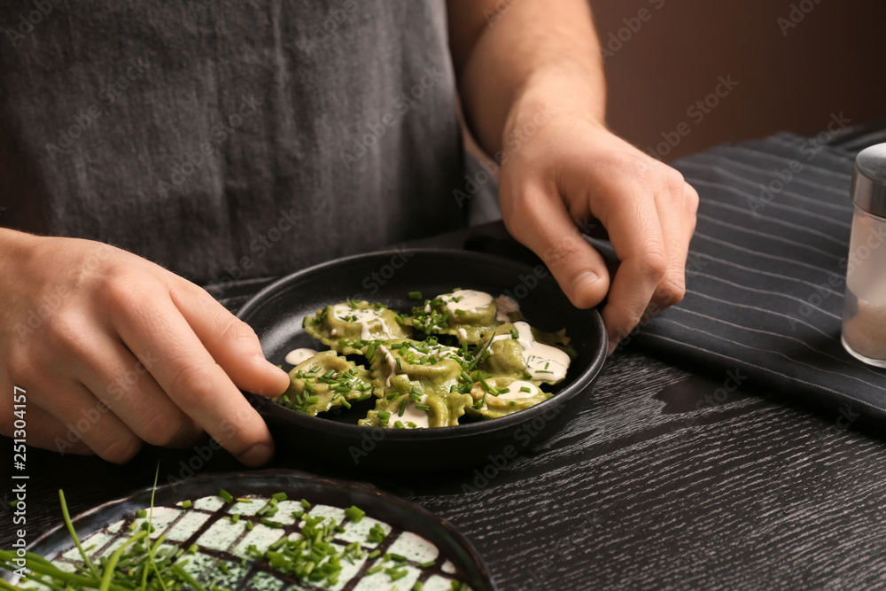 Male chef holding plate with tasty ravioli on table