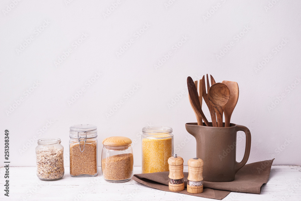 Set of kitchen utensils with groats on table near white wall