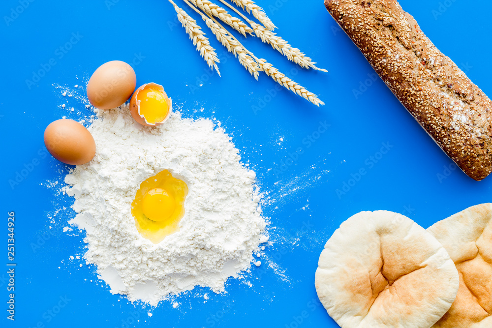 Baking background with eggs, flour and bread on blue desk. Top view.