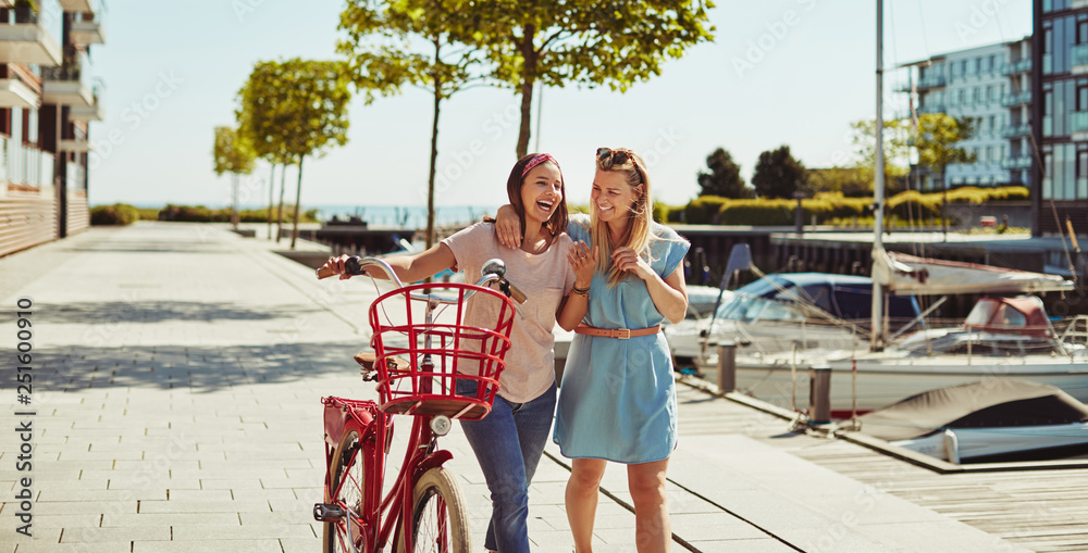 Laughing friends walking together with a bicycle through the cit