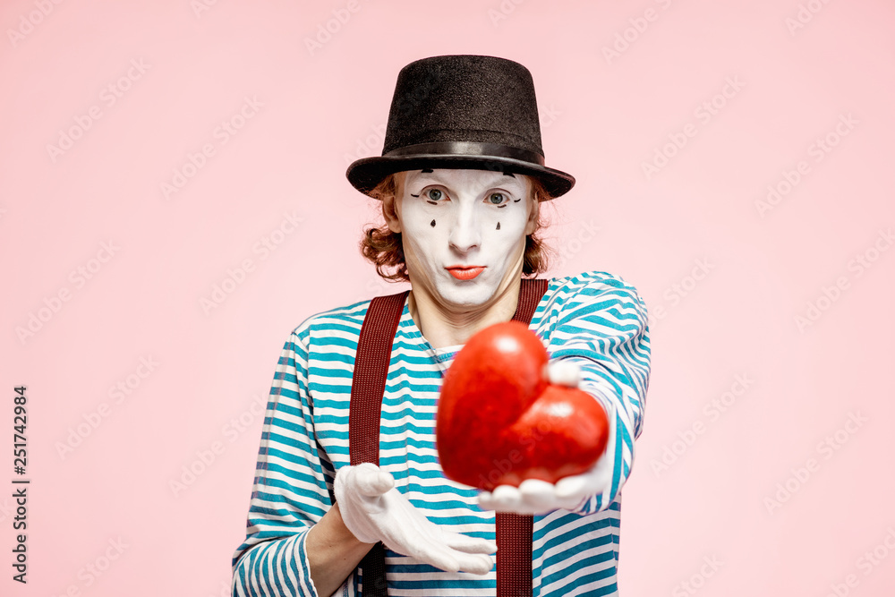 Portrait of an actor as a pantomime with white facial makeup posing with red heart on the pink backg