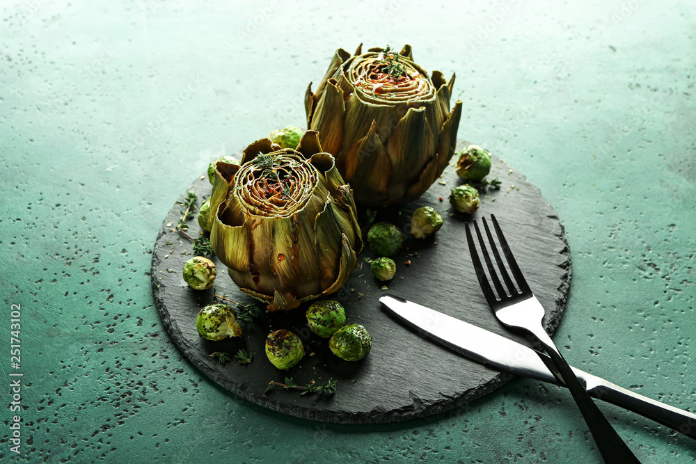 Slate plate with tasty baked artichokes and Brussels sprouts on table