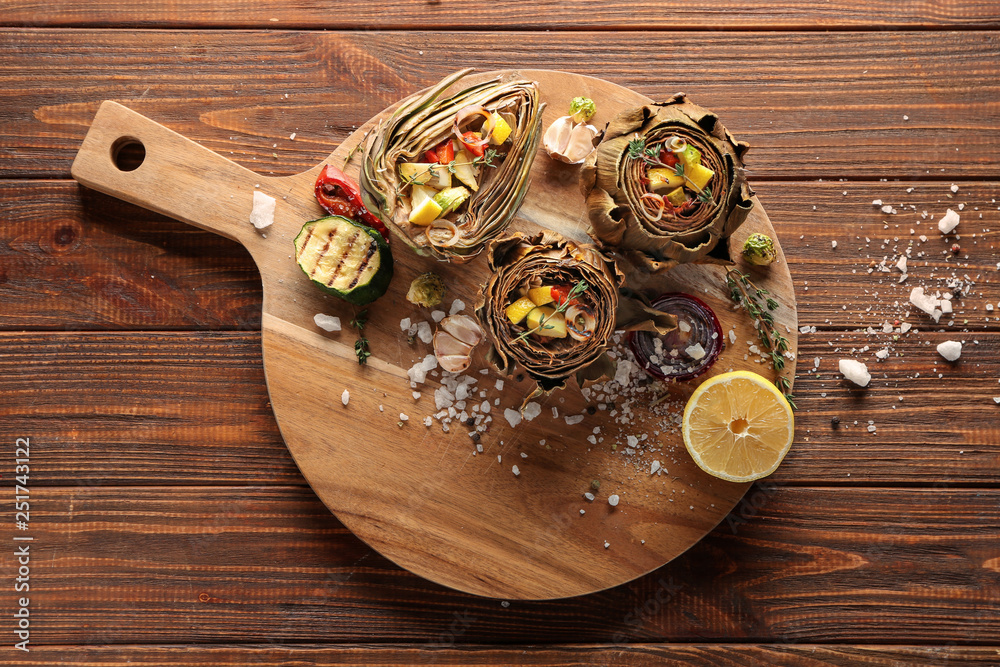 Board with tasty artichokes and vegetables on wooden table