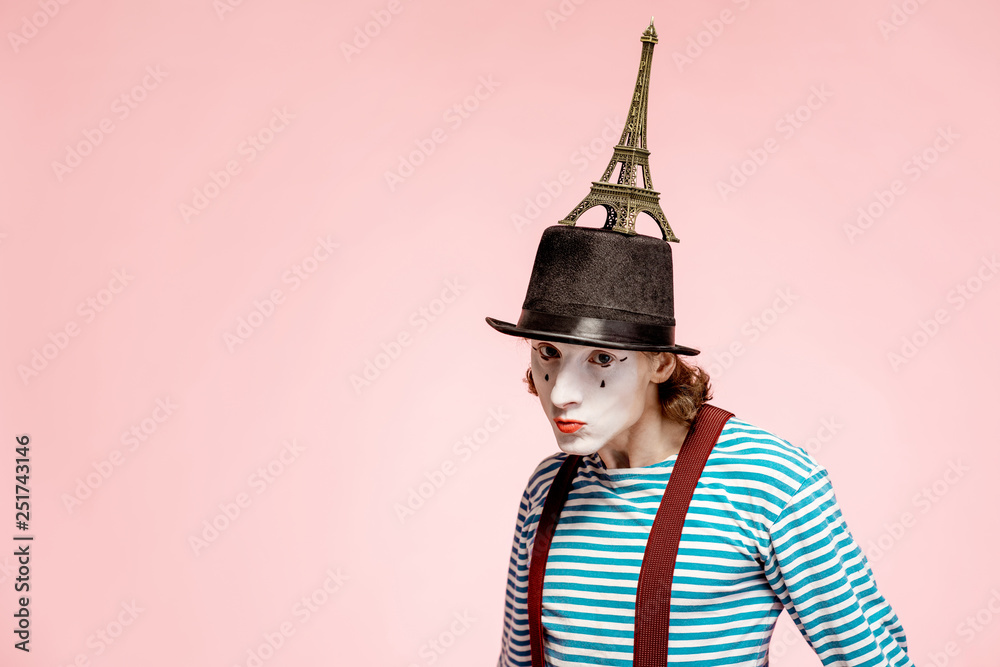 Pantomime with white facial makeup posing with Eiffel tower on the pink background. French mime conc