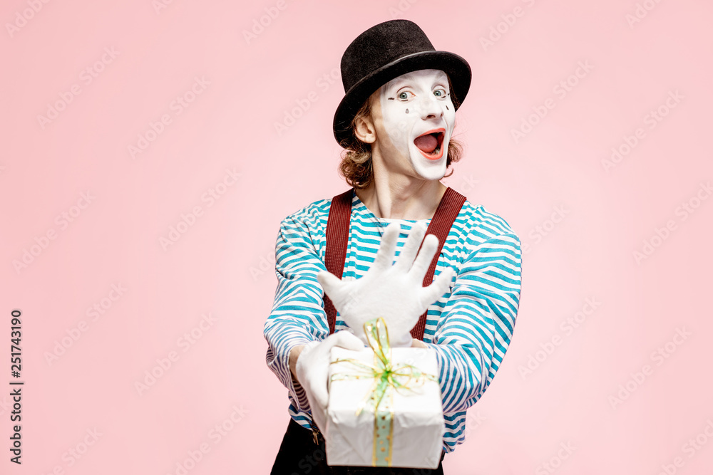 Portrait of an actor as a pantomime with white facial makeup posing with gift box on the pink backgr