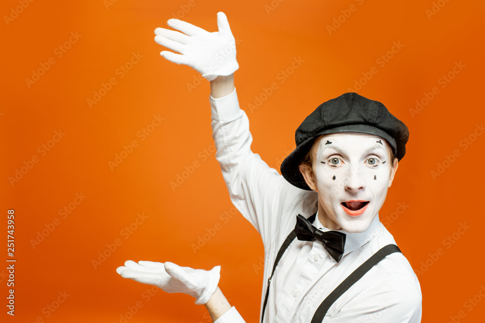 Emotional pantomime with white facial makeup showing empty space on the orange background, advertisi