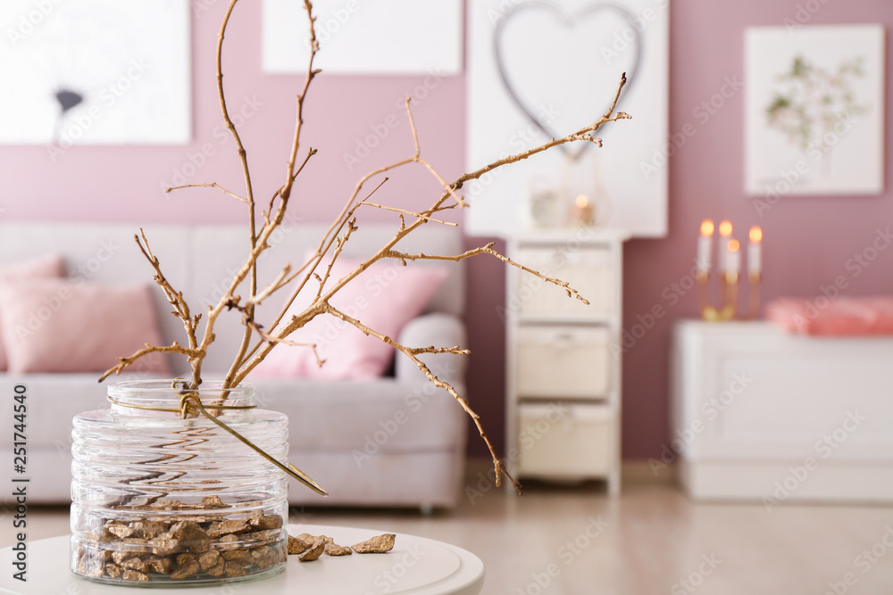 Vase with golden nuggets and tree branches on table in room