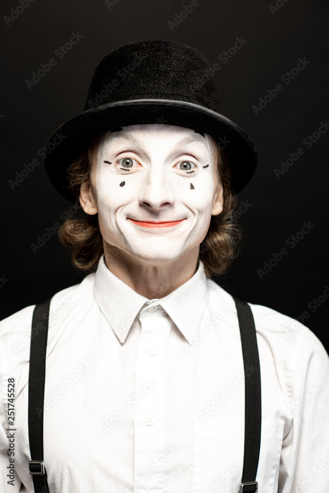 Close-up portrait of a pantomime with white facial makeup posing with expressive emotions on the bla