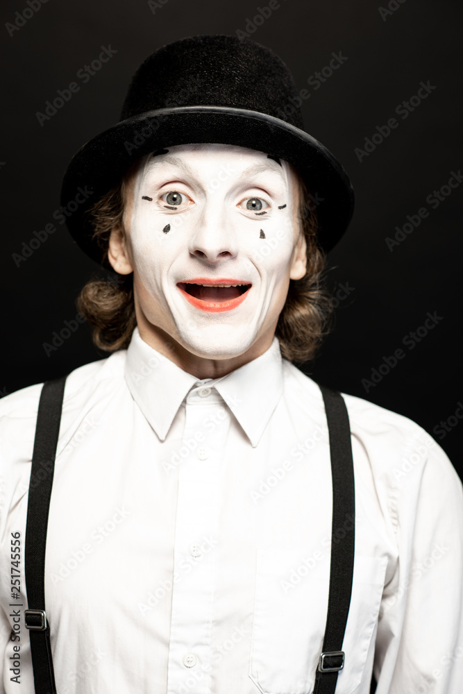 Close-up portrait of a pantomime with white facial makeup posing with expressive emotions on the bla