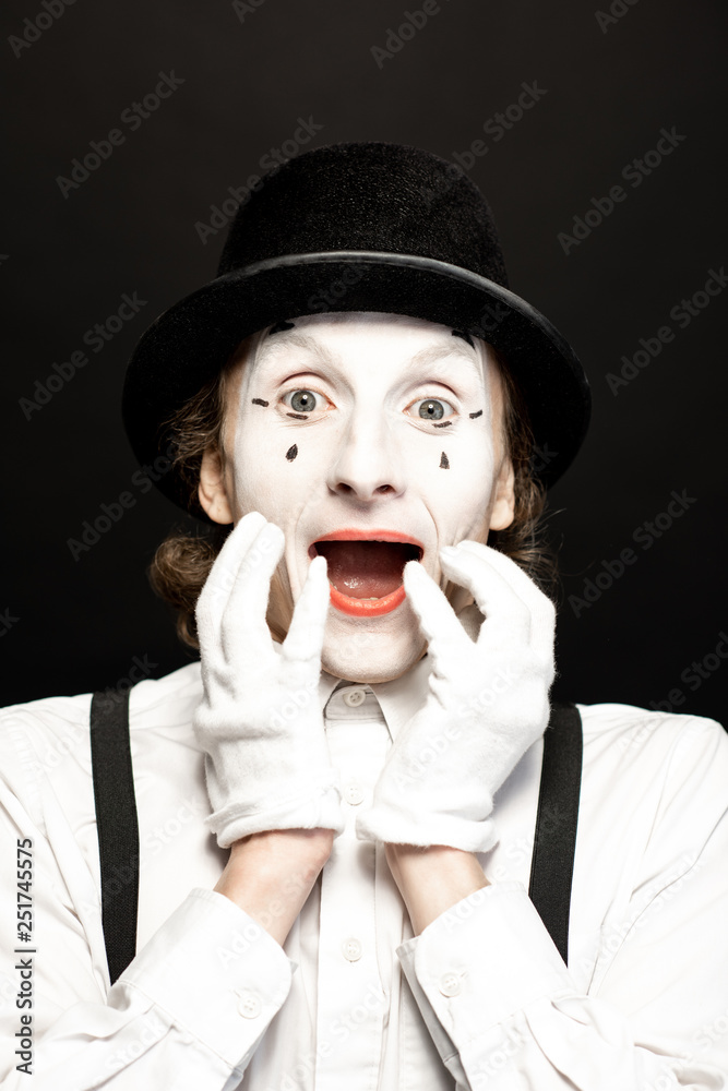 Close-up portrait of a pantomime with white facial makeup posing with expressive emotions on the bla