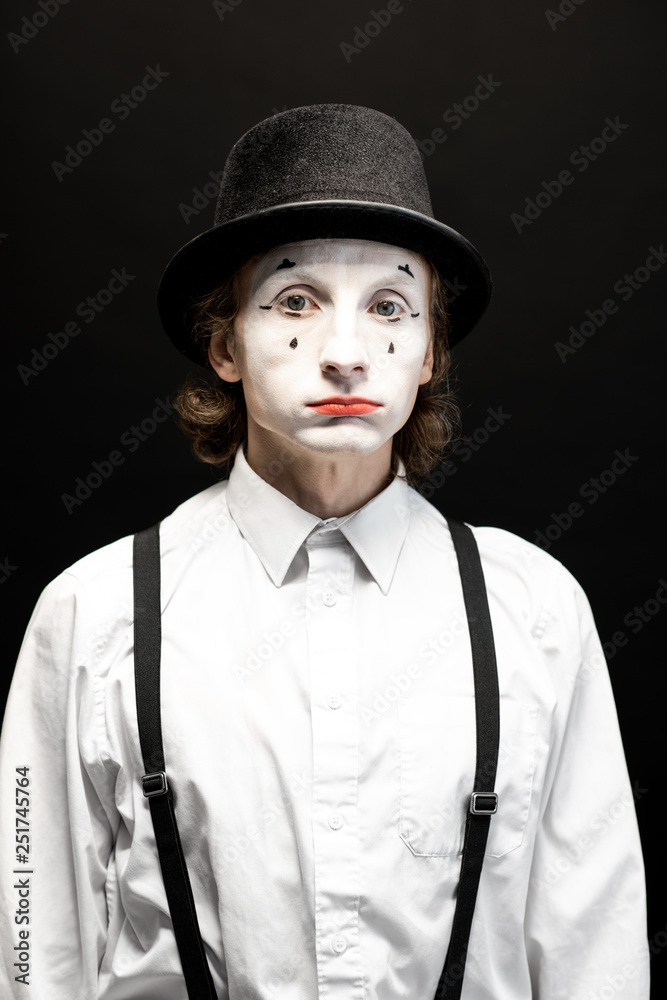 Close-up portrait of a pantomime with white facial makeup posing with expressive emotions on the bla