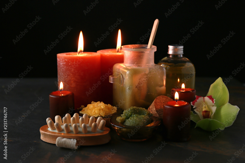 Beautiful burning candles with cosmetic products on dark table