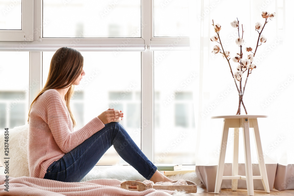 Young woman drinking hot coffee near window