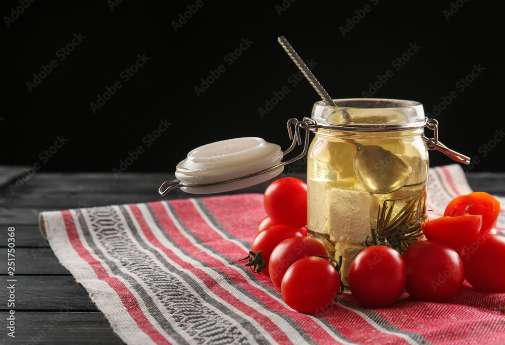 Tomatoes and glass jar with tasty feta cheese in olive oil on table