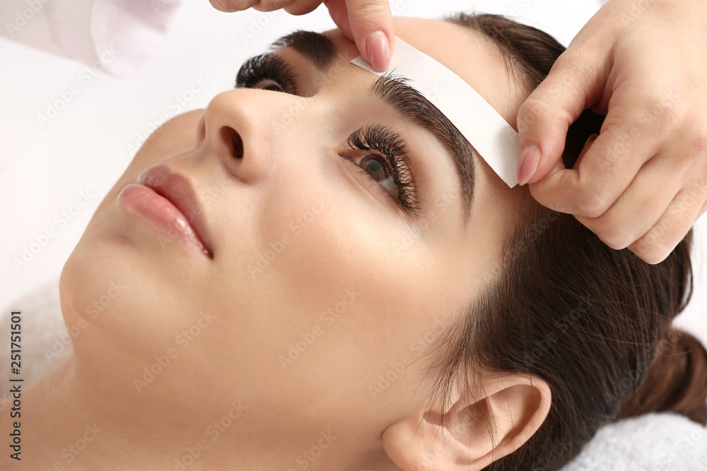 Young woman undergoing eyebrow correction procedure in beauty salon