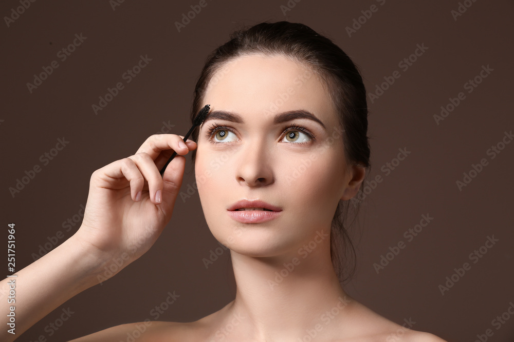 Young woman undergoing eyebrow correction procedure on color background