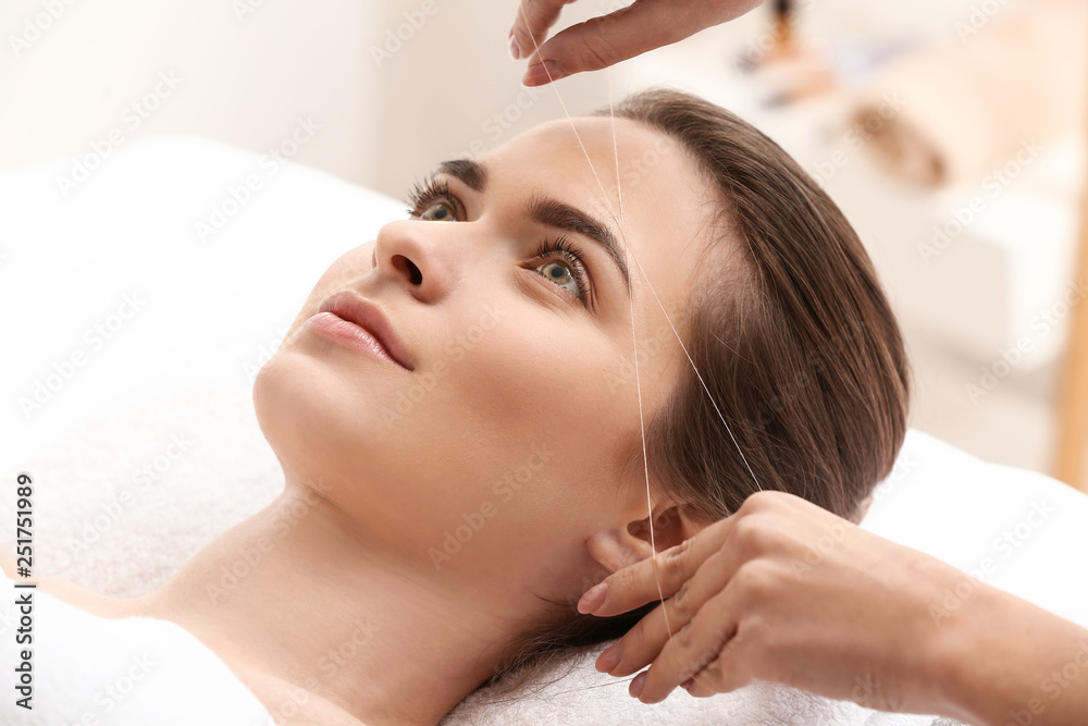 Young woman undergoing eyebrow correction procedure in beauty salon