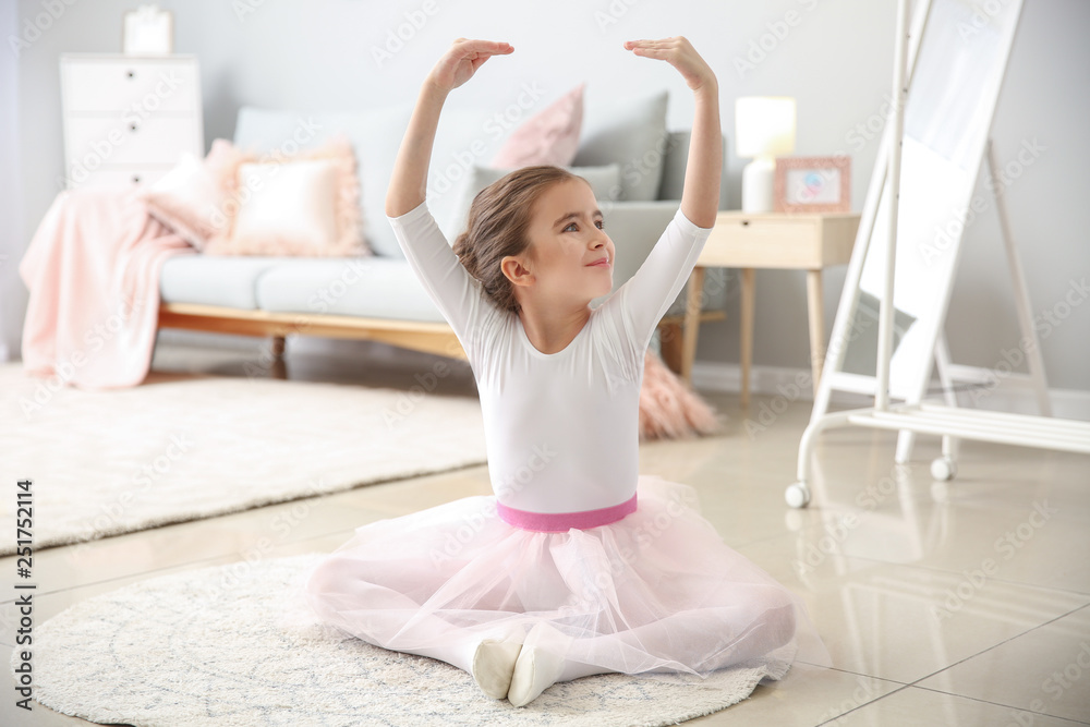 Cute little ballerina sitting on floor at home