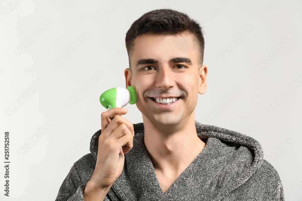 Man with facial massage tool on light background