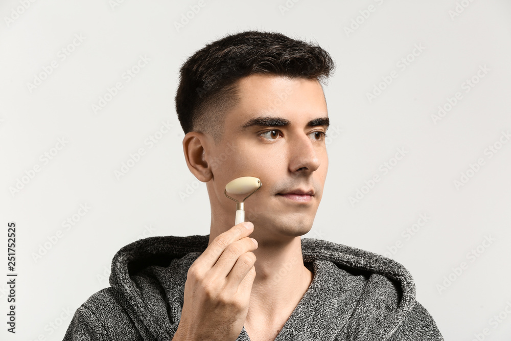 Man with facial massage tool on light background