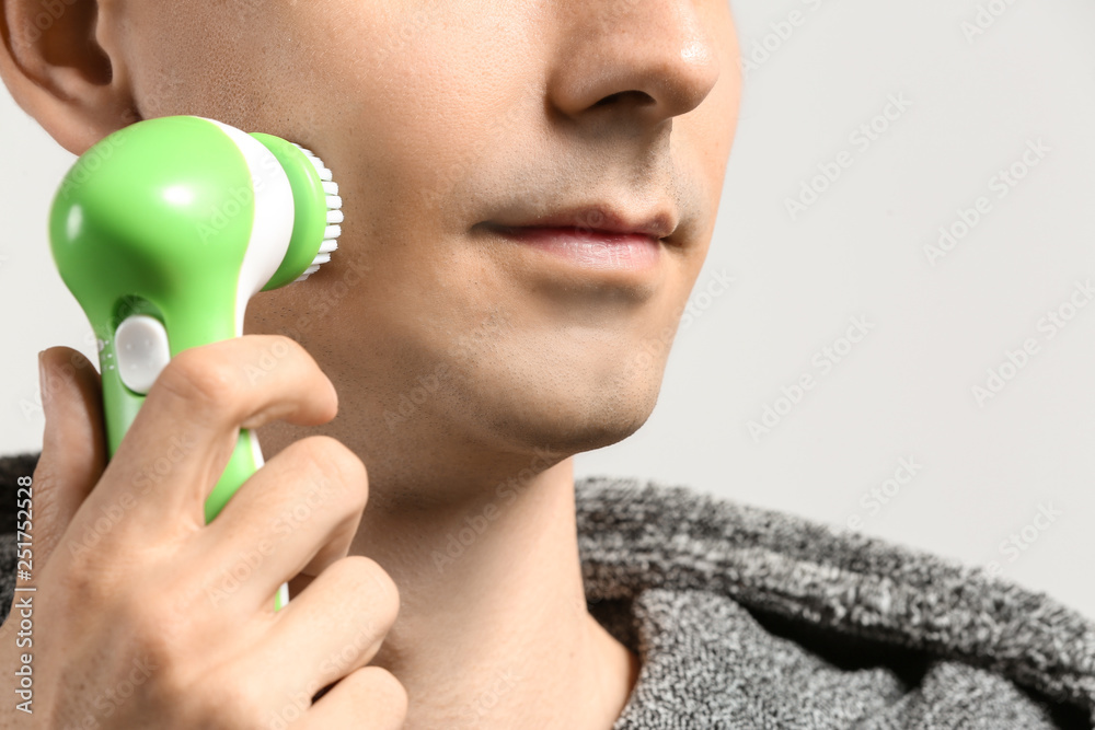 Man with facial massage tool on light background, closeup