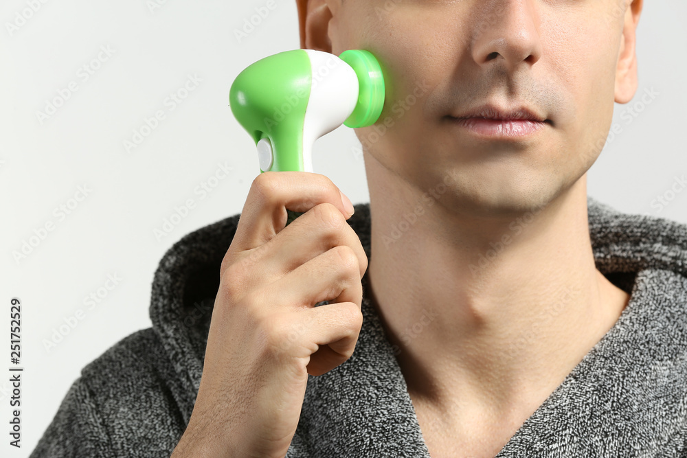 Man with facial massage tool on light background, closeup