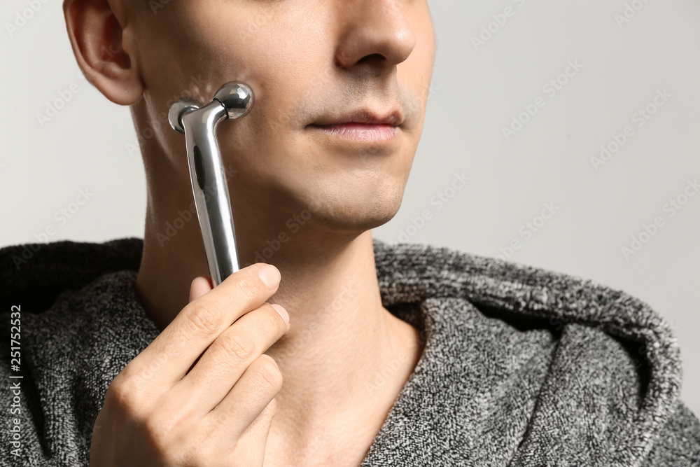 Man with facial massage tool on light background, closeup