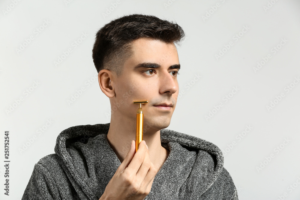 Man with facial massage tool on light background