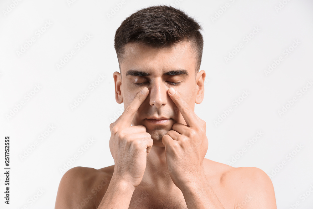 Man giving himself face massage on light background