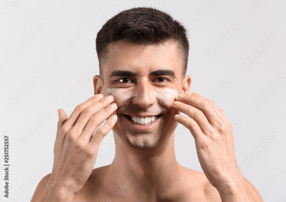 Man with applied face serum giving himself face massage on light background