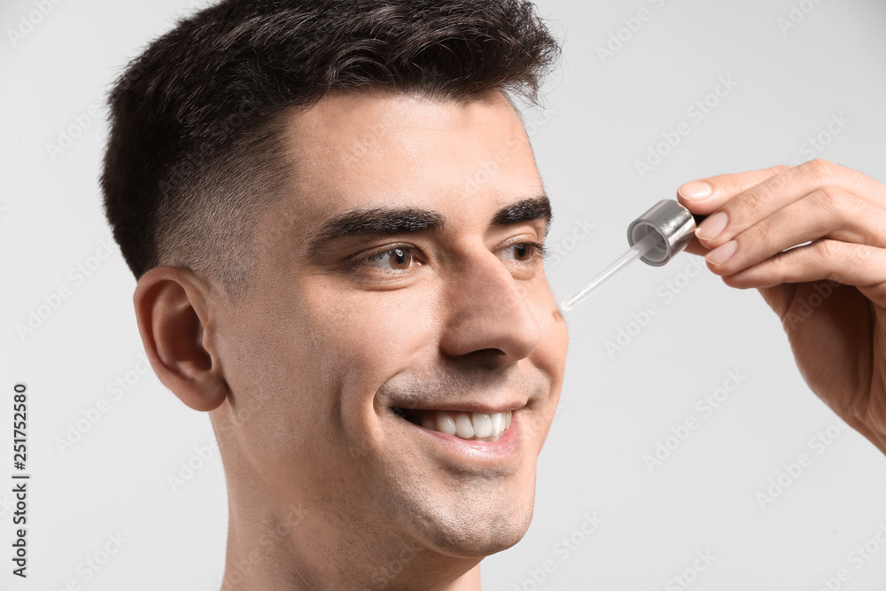 Handsome man applying face serum on light background