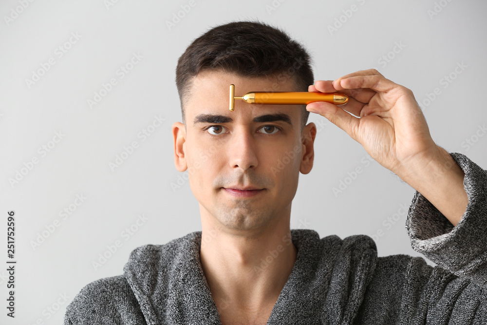 Man with facial massage tool on light background