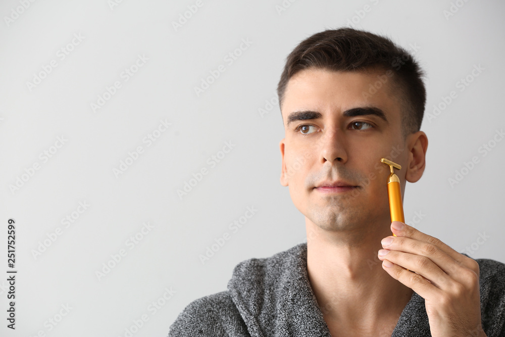 Man with facial massage tool on light background