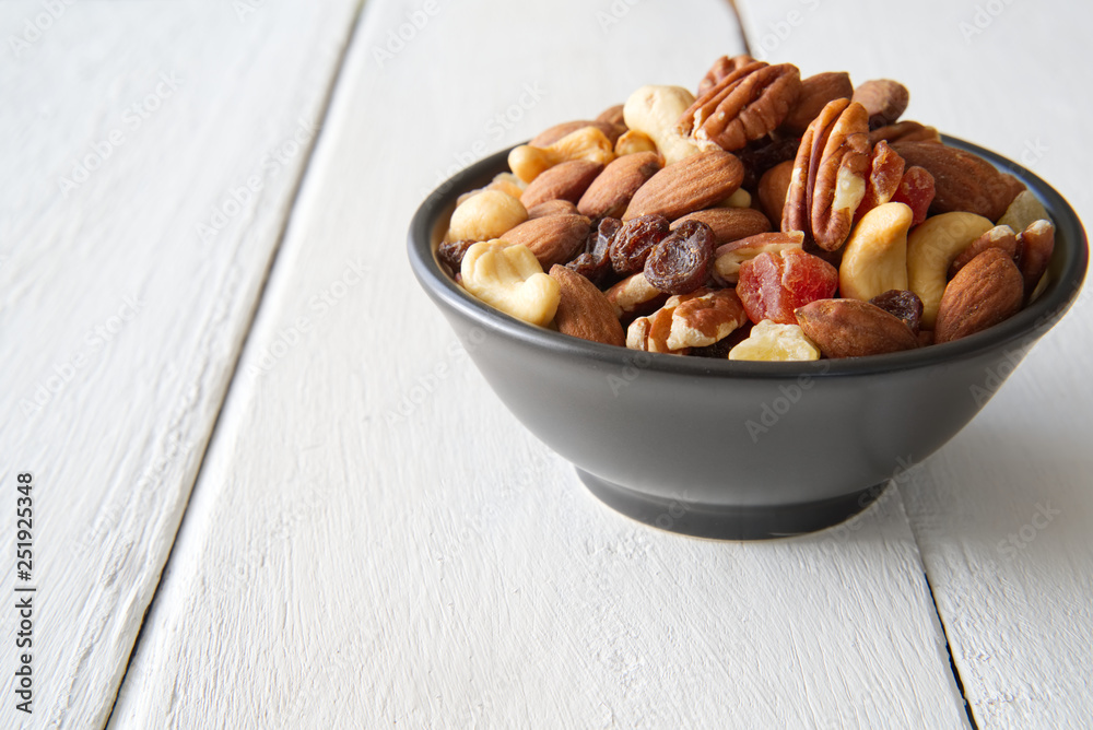 Mix nuts and dried fruits in the bowl put on the white painted wooden. Seen from side view. Food and