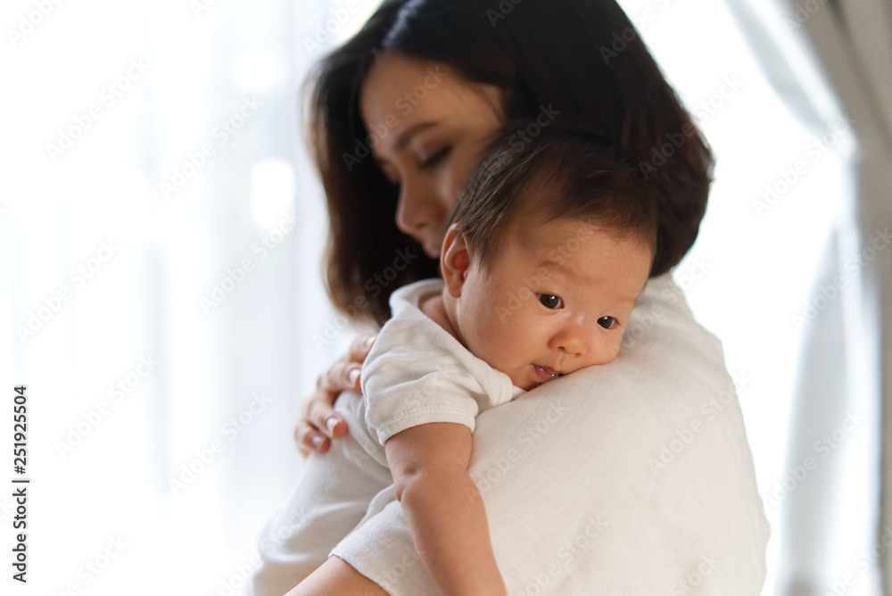 亚洲年轻母亲把刚出生的婴儿抱在肩上，把手放在婴儿背上