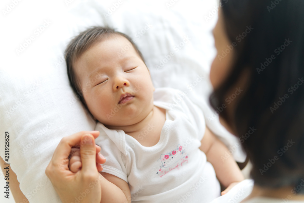 Asian young mother holding her newborn baby hand while the child is sleeping on white pillow. Seen f