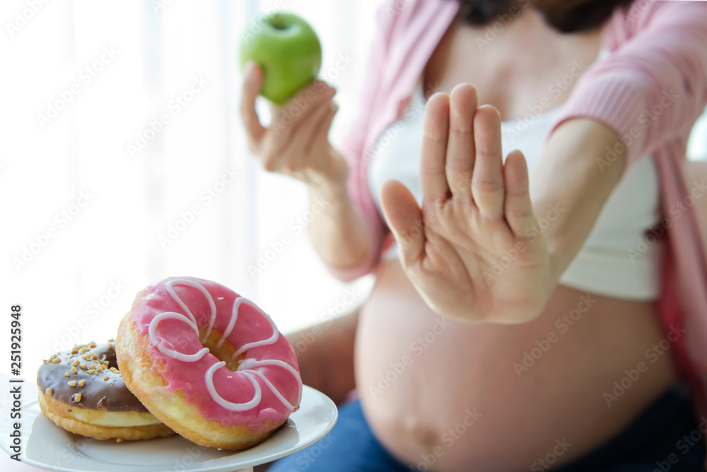 Dieting pregnancy woman refusing her favorite junk food such as donuts and choosing green apple inst