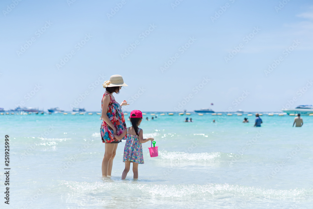 亚洲年轻母亲和她的孩子站在海滩上眺望大海。母亲抱着他